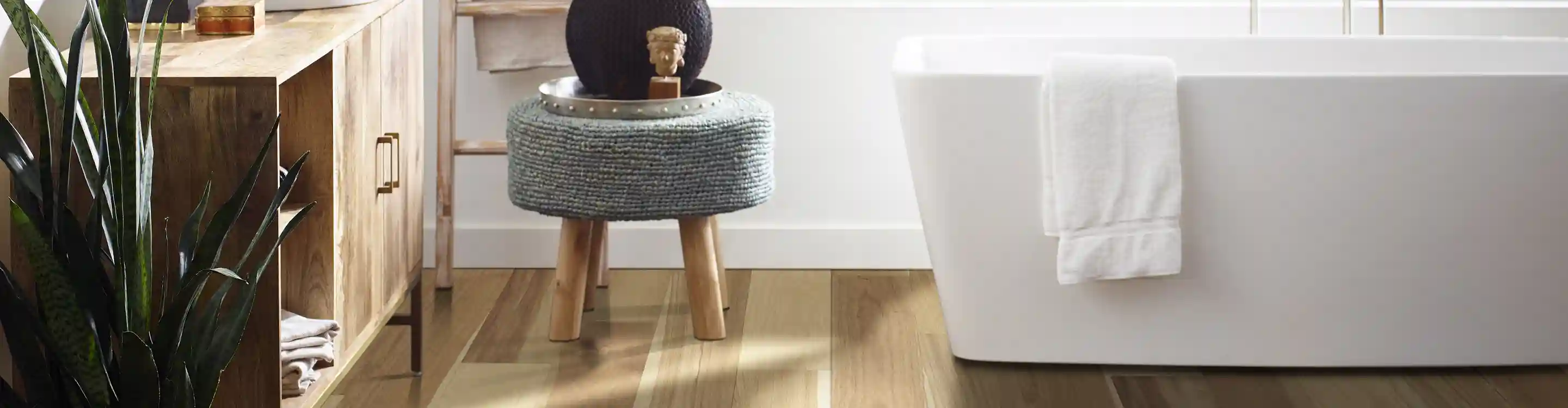 white soaker tub in open bathroom with light wood flooring and grey footstool